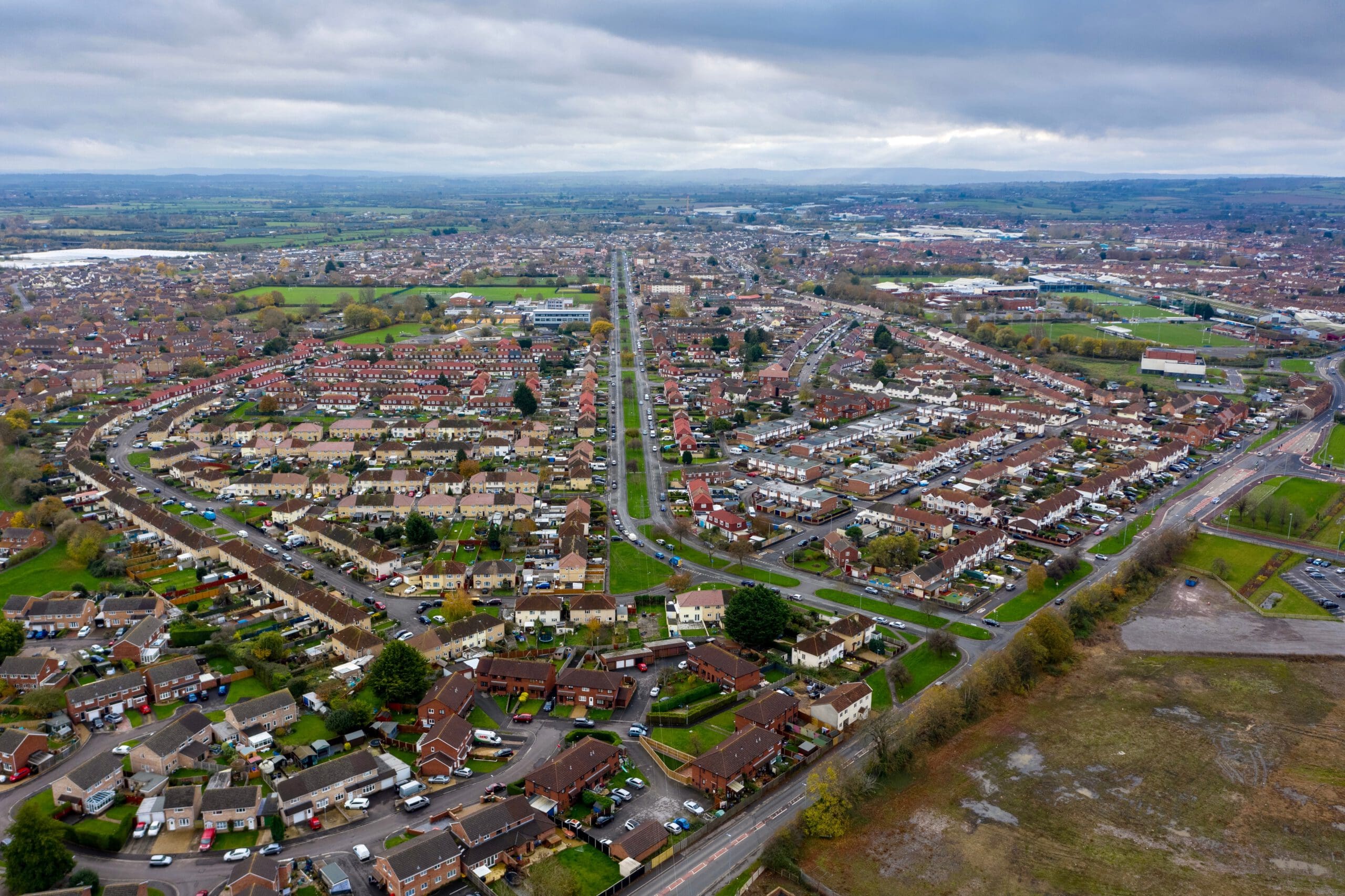 Aerial view of a suburban neighborhood with rows of houses, intersecting roads, green spaces, and fields under a cloudy sky—ideal for homeowners considering sash window repairs or hiring a painter and decorator to enhance their properties.